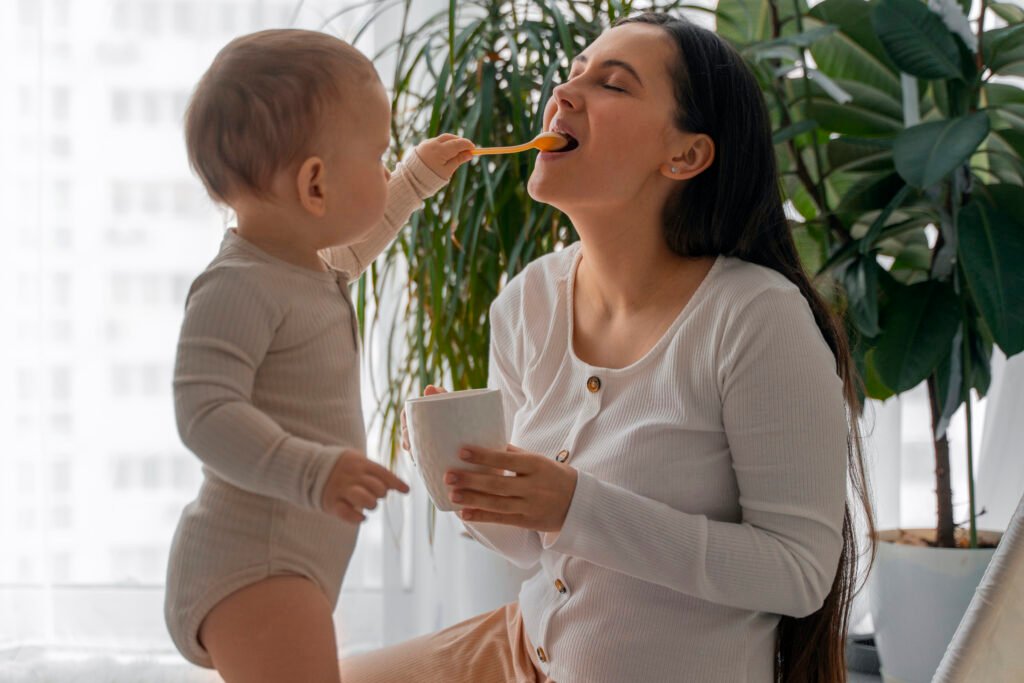 Baby playfully feeding their mother with a spoon, reflecting the shared connection in a baby-led and spoon-fed approach.